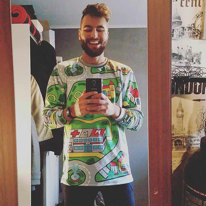 Man wearing a colorful sweater with graphic designs, standing indoors.